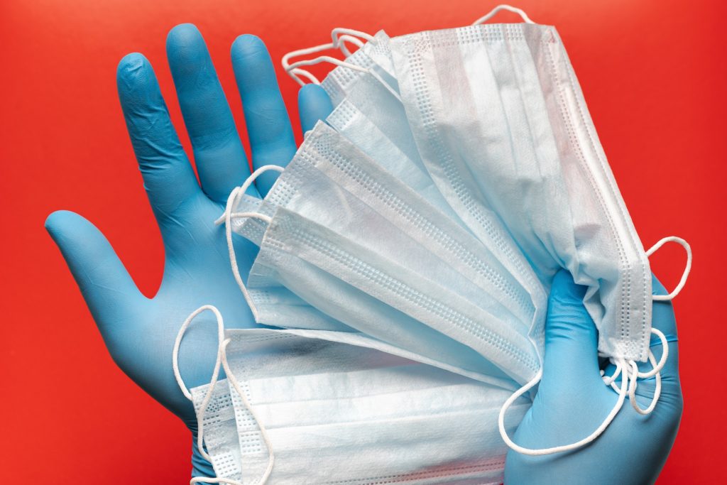 A pair of hands wearing protective rubber gloves holding a bunch of thin surgical masks