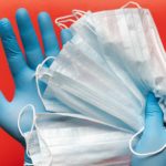 A pair of hands wearing protective rubber gloves holding a bunch of thin surgical masks